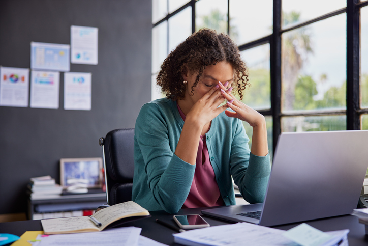 Adult with ADHD overwhelmed at a cluttered desk, holding their head in their hands.